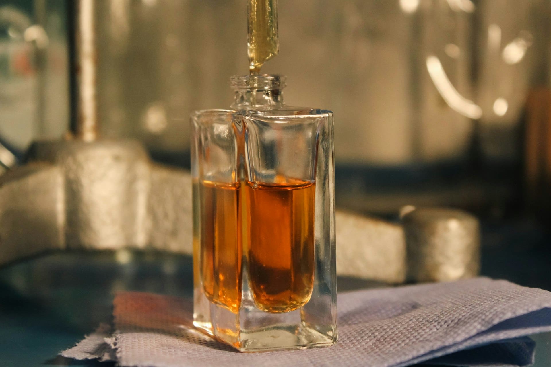 A pipette dripping amber perfume oil into a small glass bottle at a perfumer's bench